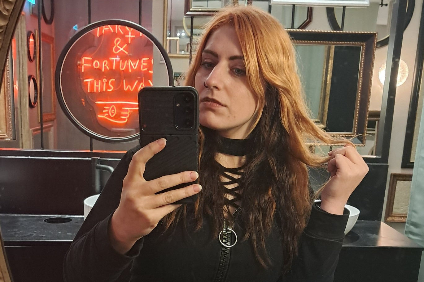 Woman taking a mirror selfie in a room with neon signs.