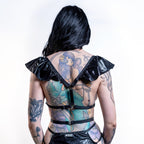 Person wearing a black chest harness with ruffled straps on a white background