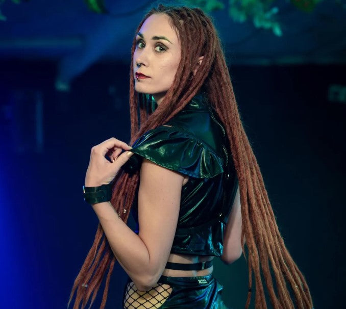 Woman with long braided hair wearing a chest harness against a dark background
