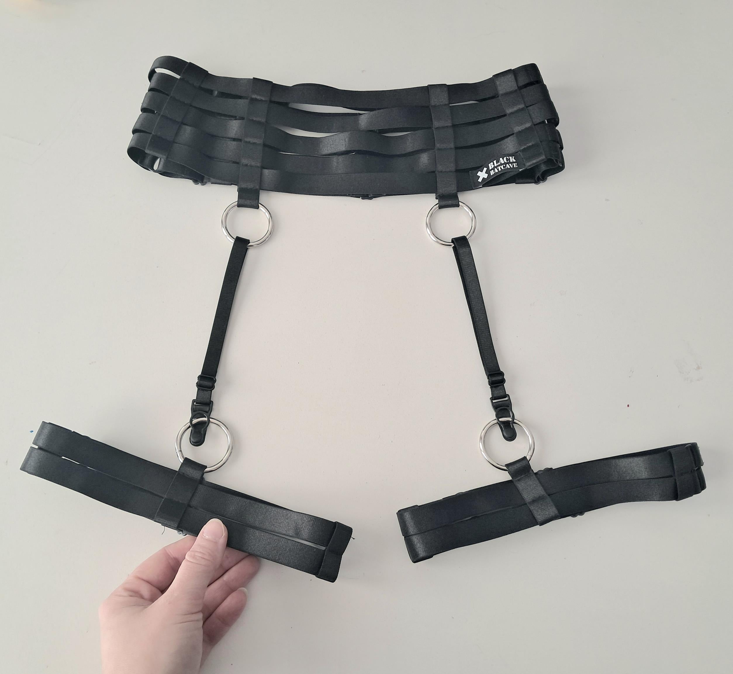 Black satin shine strappy garter belt with metal rings on a white background