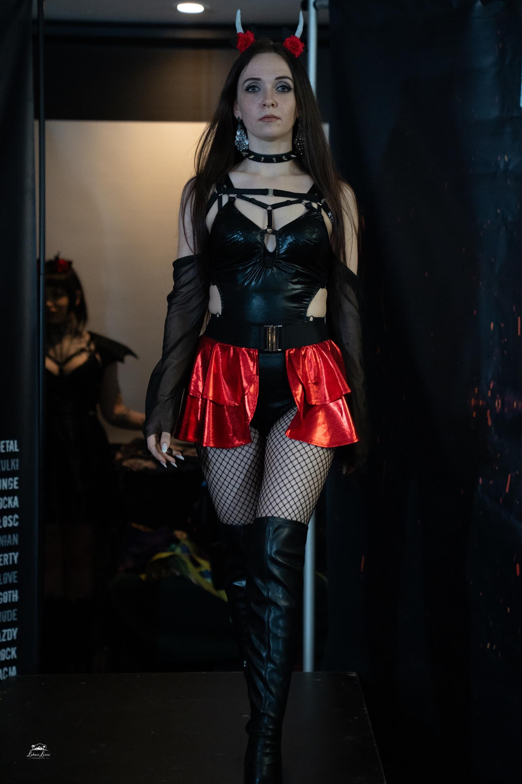 Person wearing a black bodysuit and red skirt with fishnet stockings and high boots.