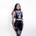 Woman wearing a black wet look mini skirt with suspenders with intricate designs on a white background