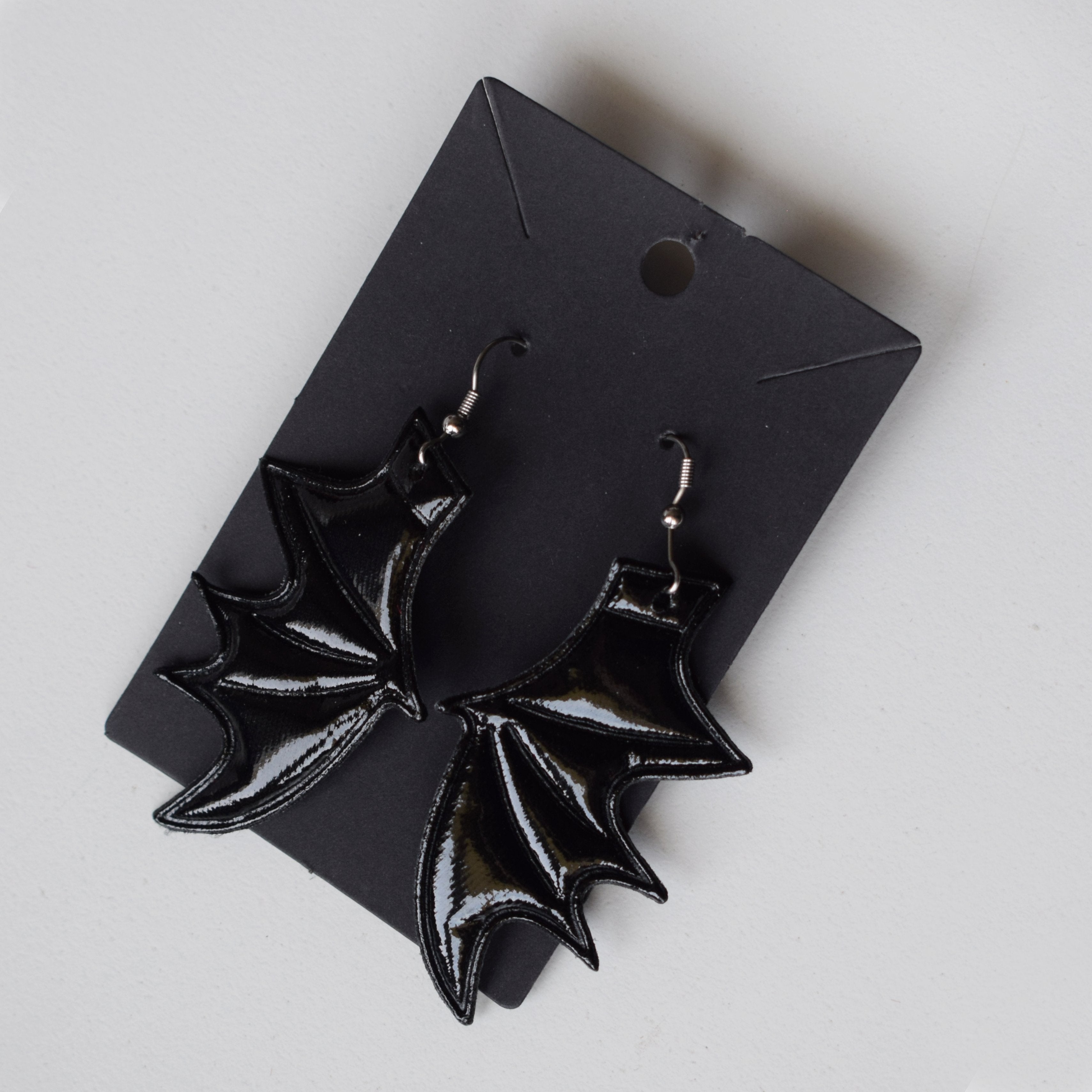 Black bat-wing earrings on a black card against a white background