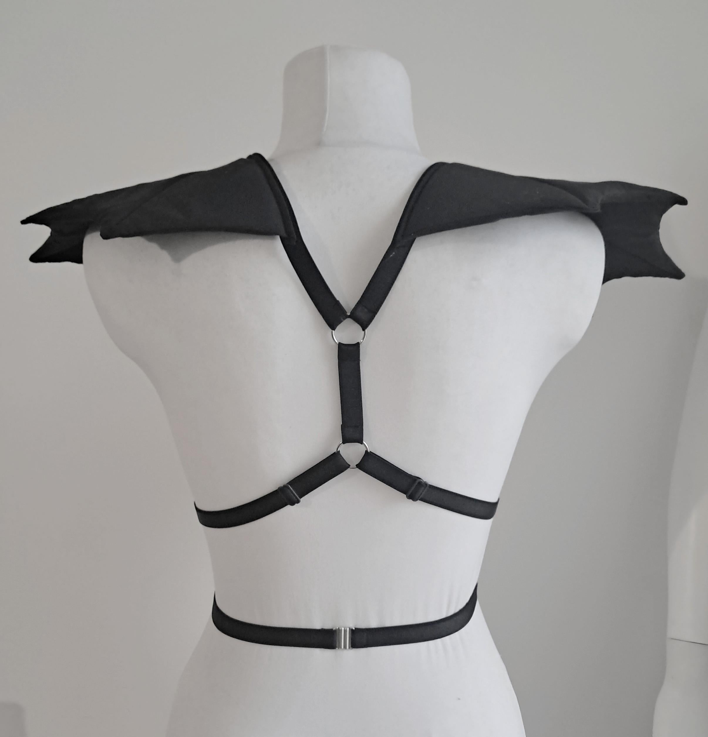 Black harness with bat wings epaulets on a mannequin against a gray background