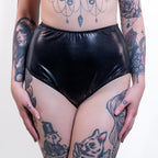Person wearing black wet-look high waist panties with tattoos on arms and legs.