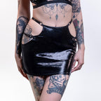 Person wearing a black wet-look cut-out mini skirt with cut-out design on a white background