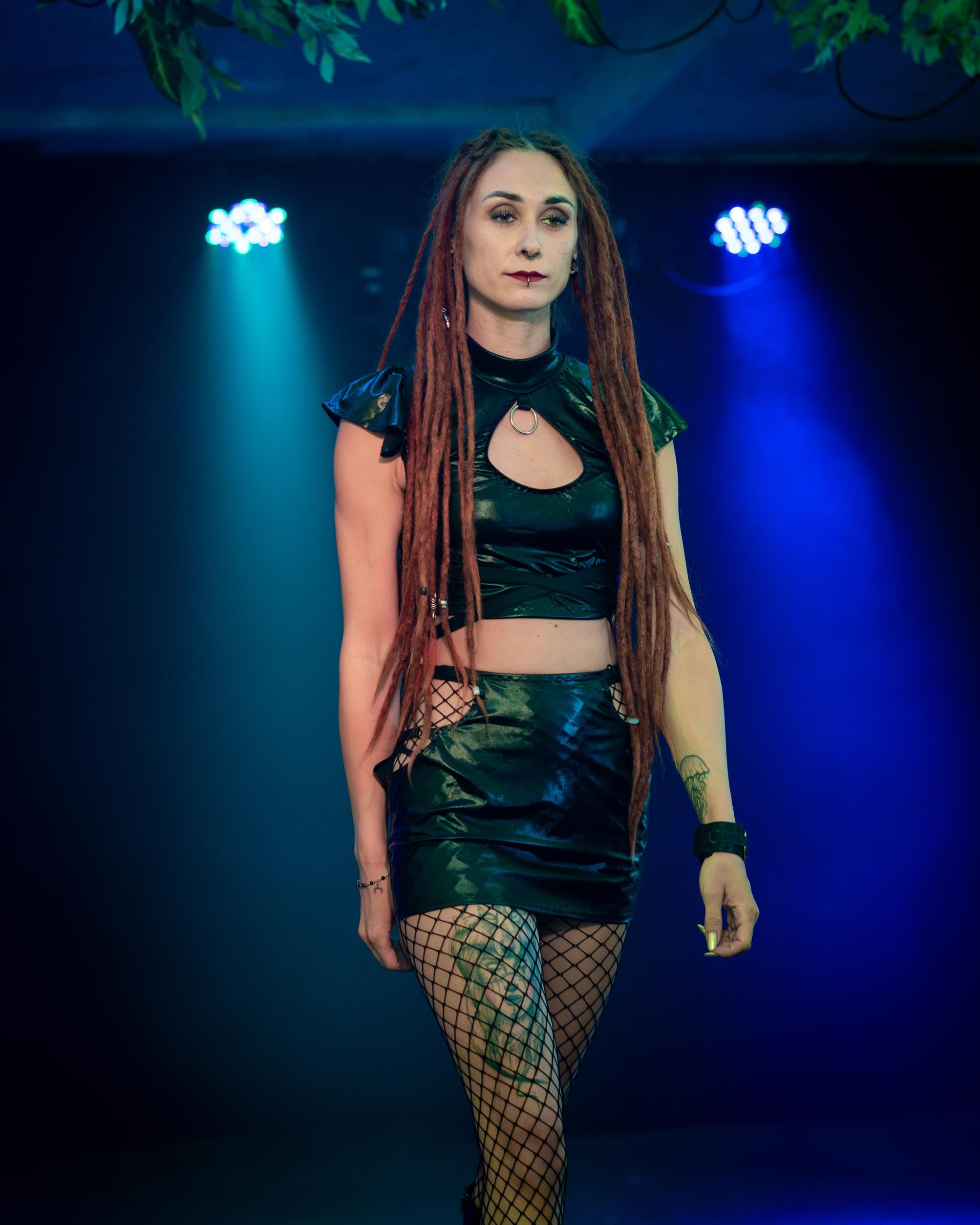 Woman in a wet-look cut-out mini skirt  with fishnet stockings against a blue background