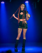 Person in awet-look cut-out mini skirt with fishnet stockings and black boots against a blue background