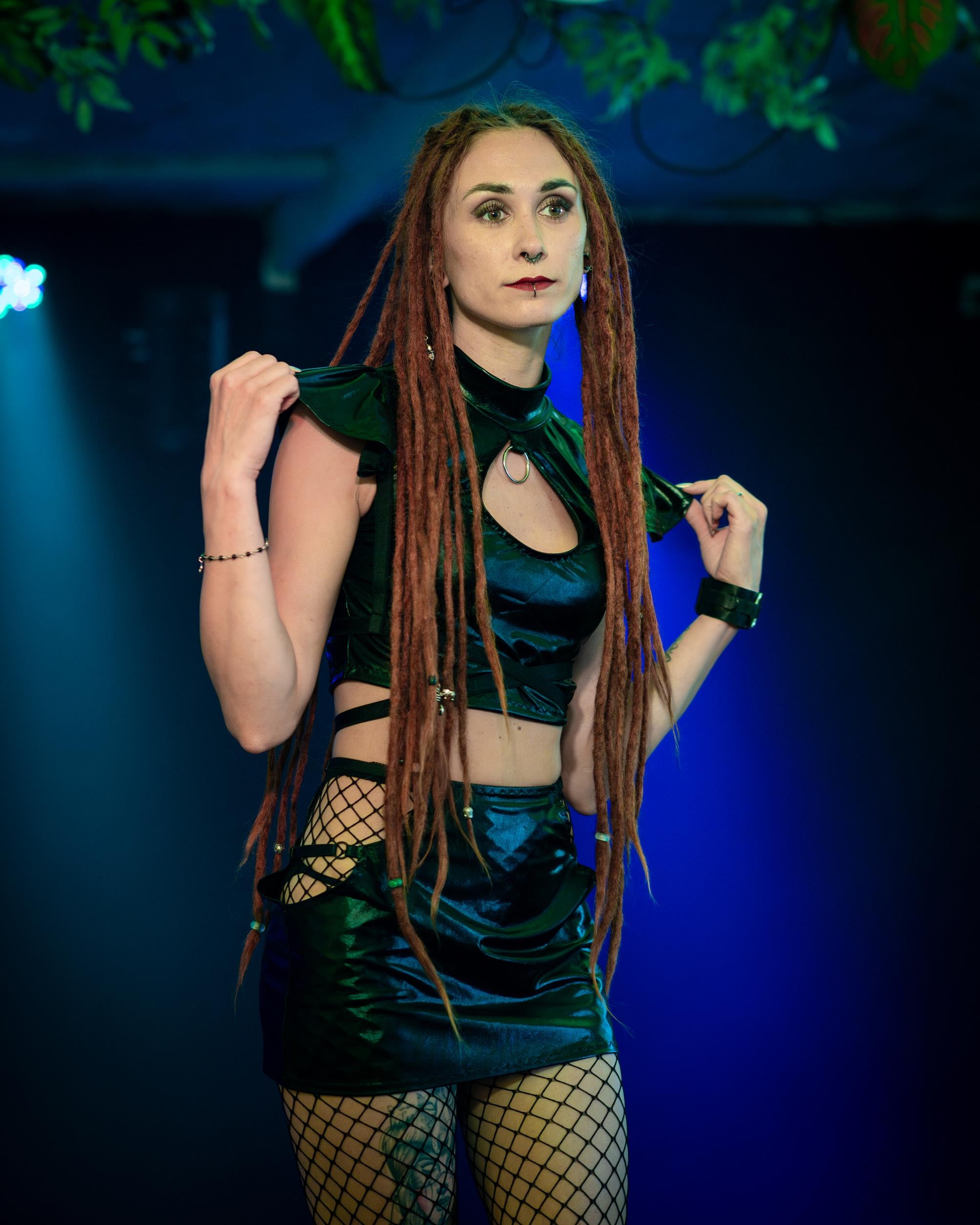 Woman in a wet-look cut-out mini skirt with fishnet stockings against a dark background