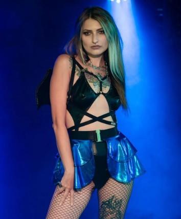 Person wearing a black and blue wet-look open front mini skirt with fishnet stockings against a blue background