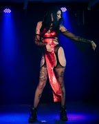 Person wearing a red wet look cut-out dress with tattoos on a dark background