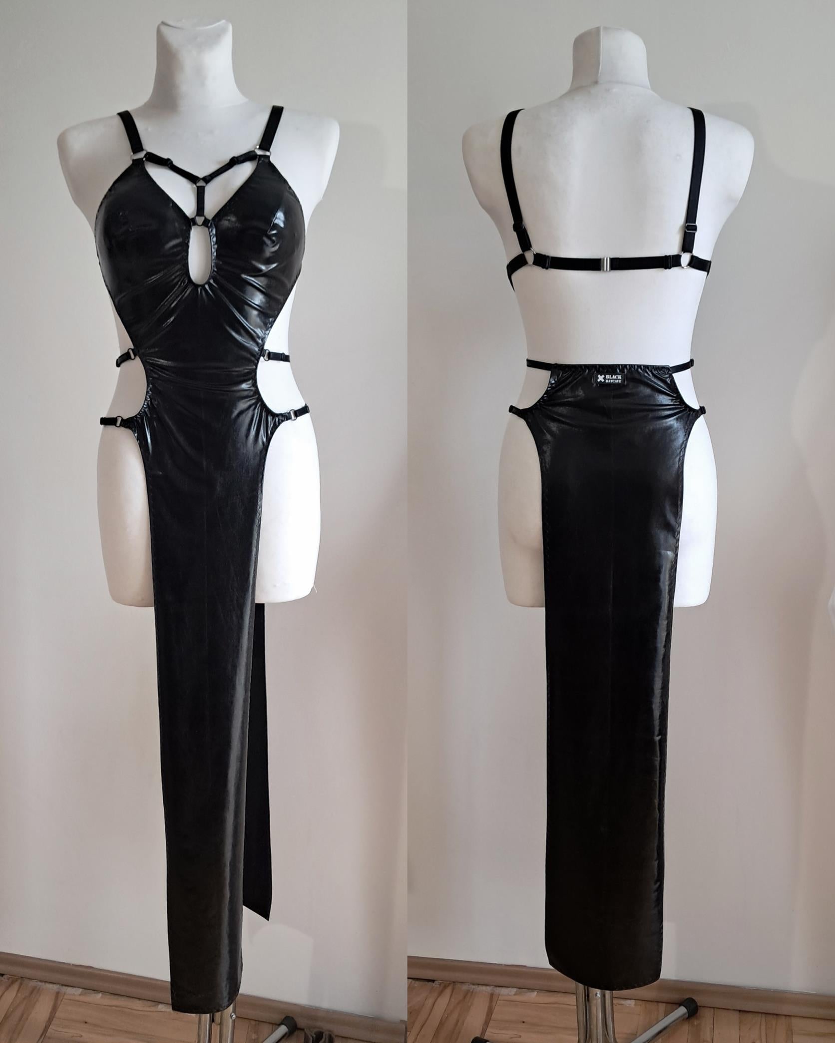 Black wet look dress on a mannequin with cut-out design against a plain background