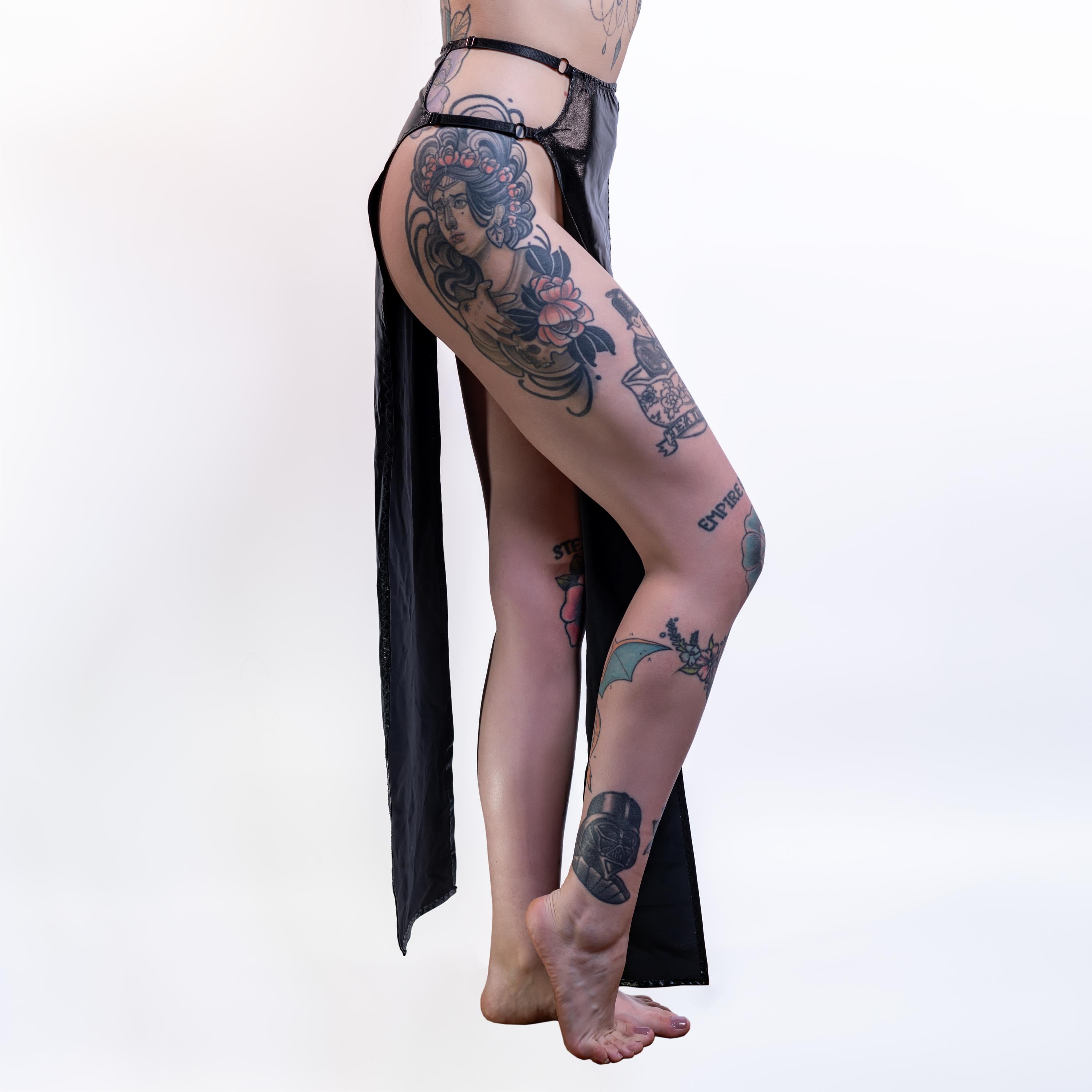 Person wearing black wet-look cut-out maxi skirt with tattoos on a white background