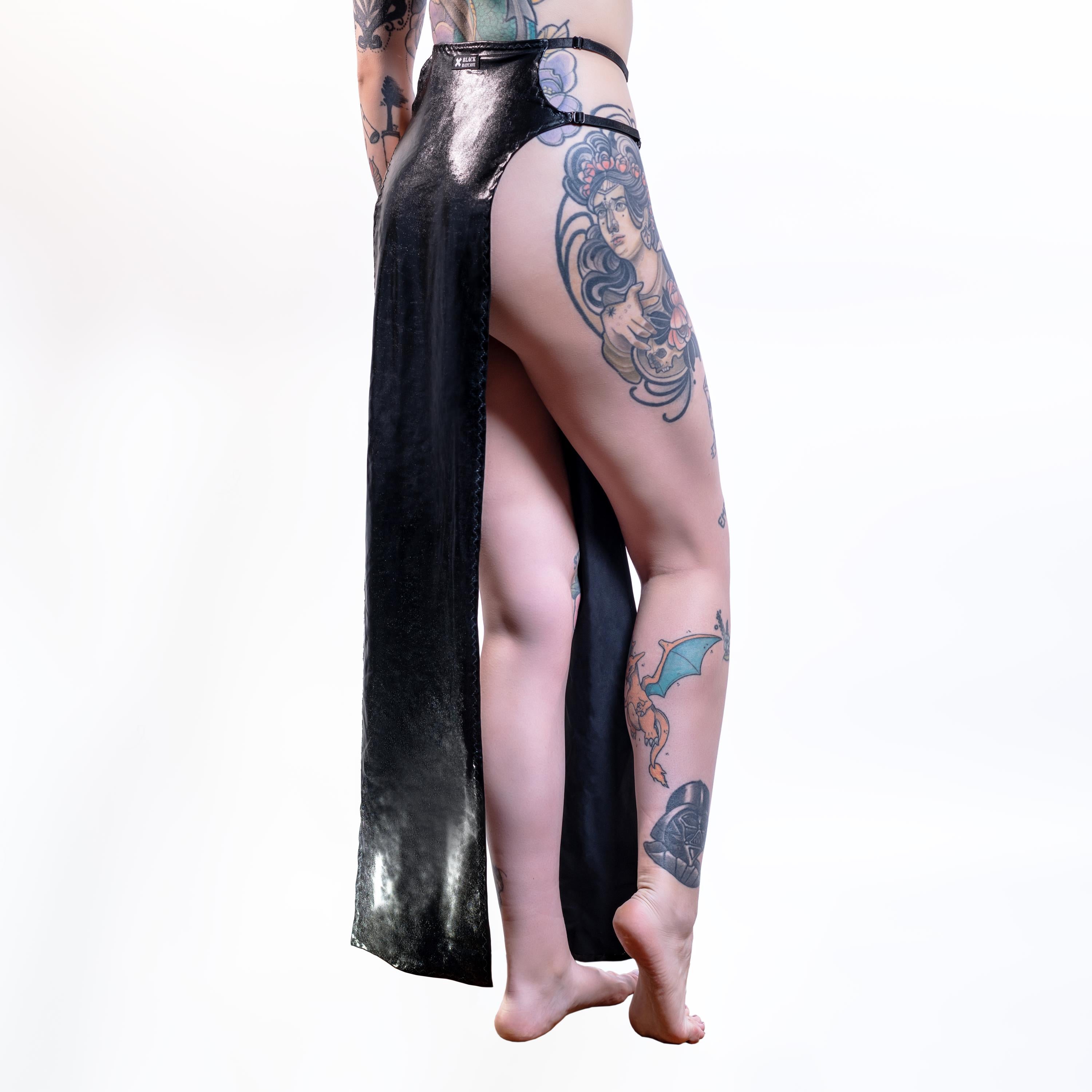 Person wearing a black wet-look cut-out maxi skirt with tattoos on a white background