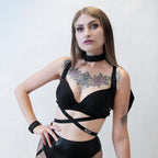 Woman wearing a black harness with bat wings with tattoos on a plain background