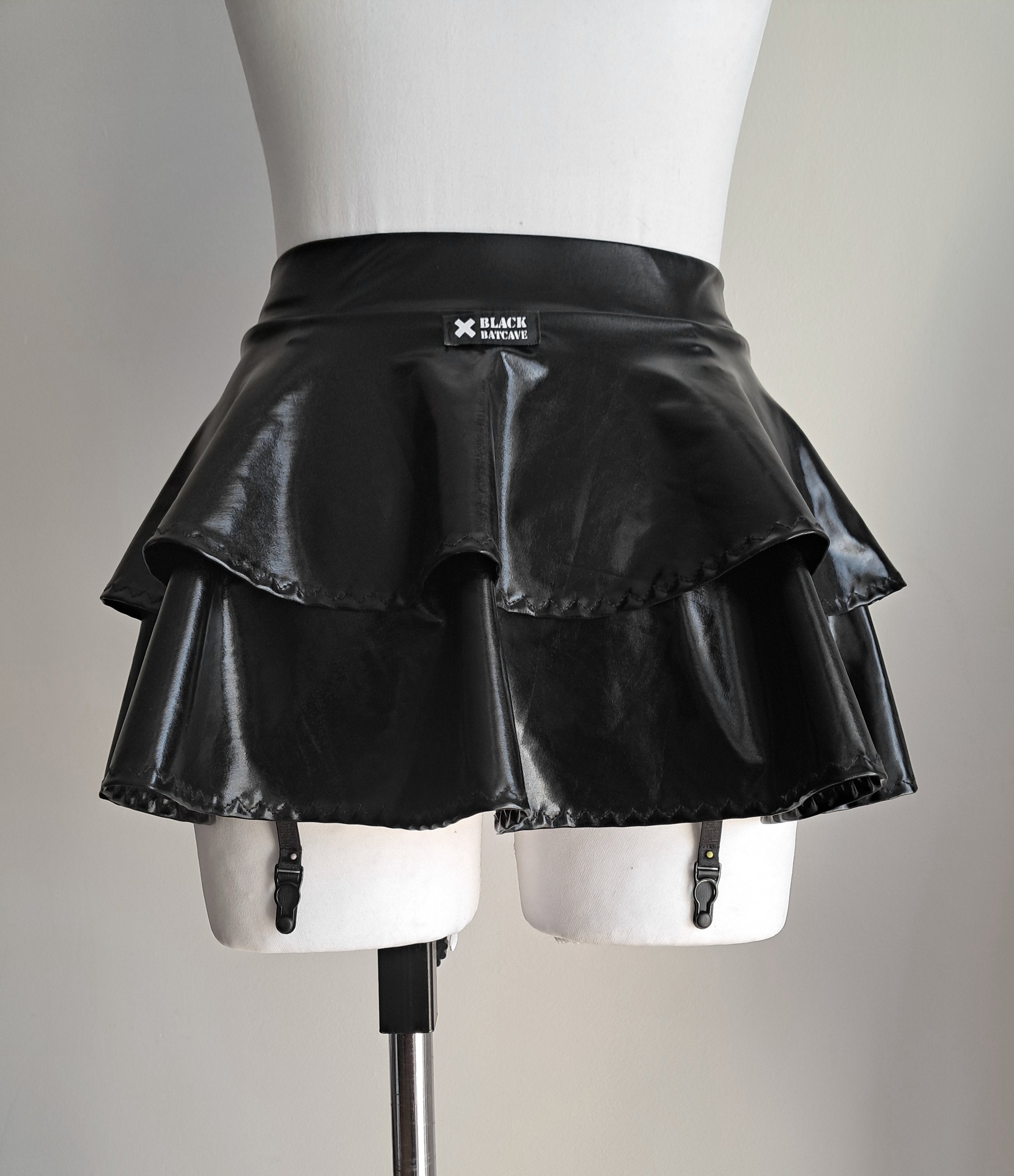 Black wet-look mini skirt with suspenders on a mannequin against a plain background