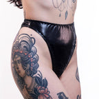 Person wearing black wet look high waist thong with tattoos on arms and legs.