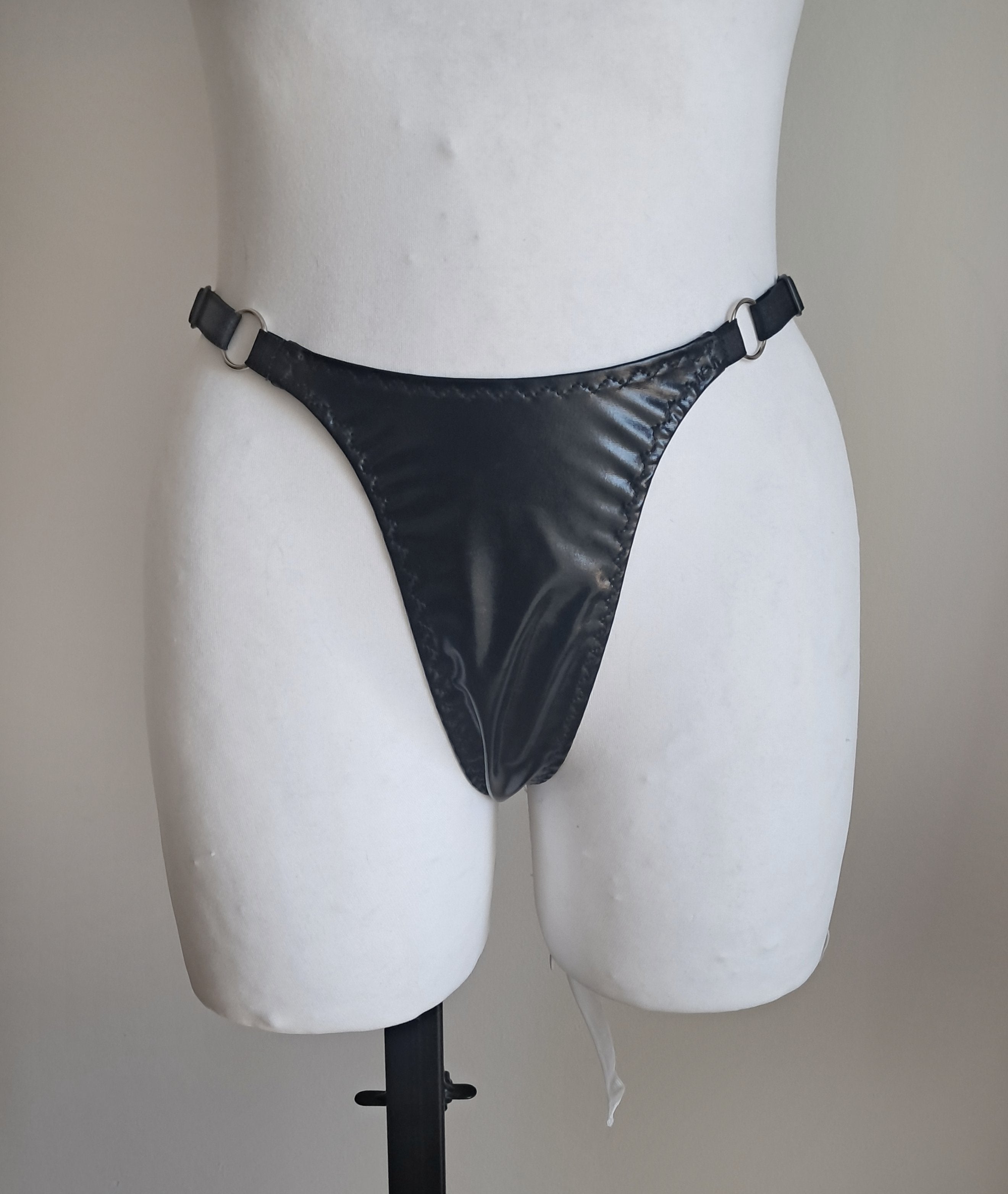 Black strappy wet look thong on a mannequin against a plain background