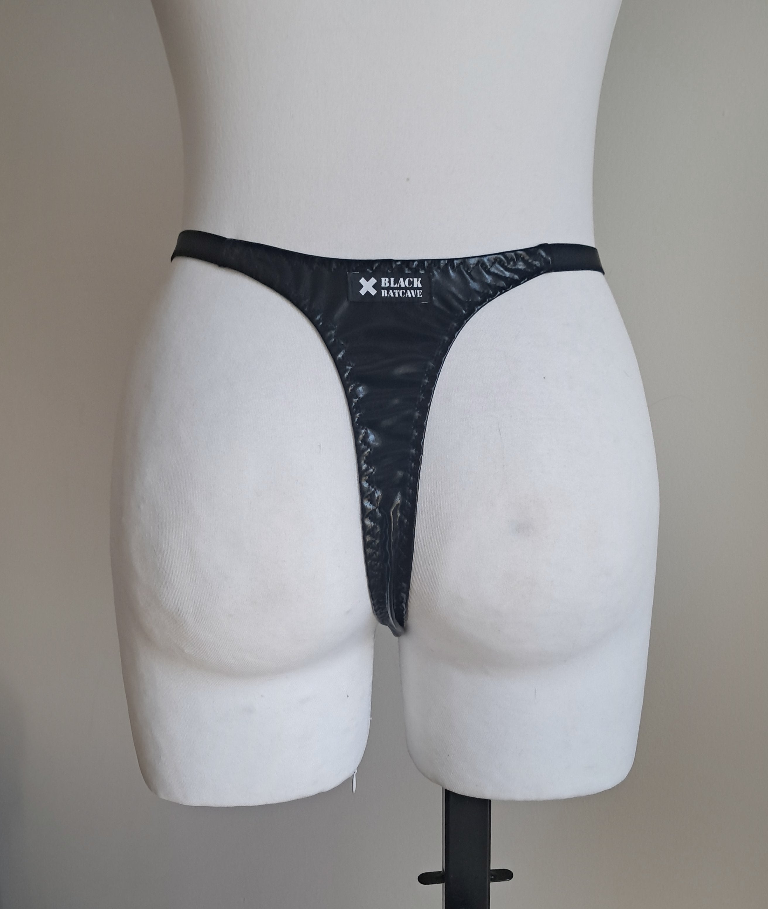 Black strappy wet look thong on a mannequin against a plain background