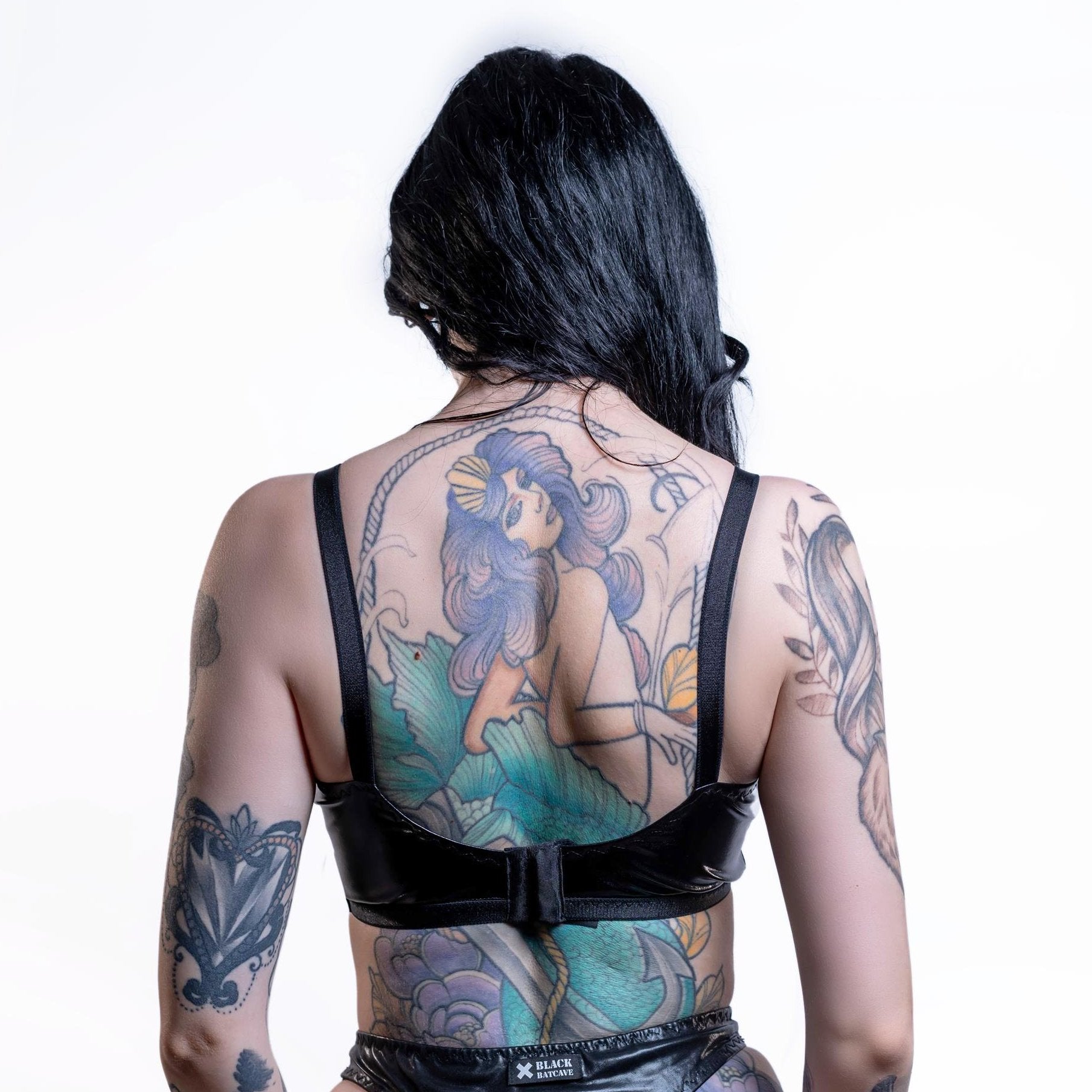 Person wearing a black wet look bra  with mermaid tattoo design on a white background
