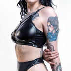 Person wearing a black wet look bra with visible tattoos on a white background