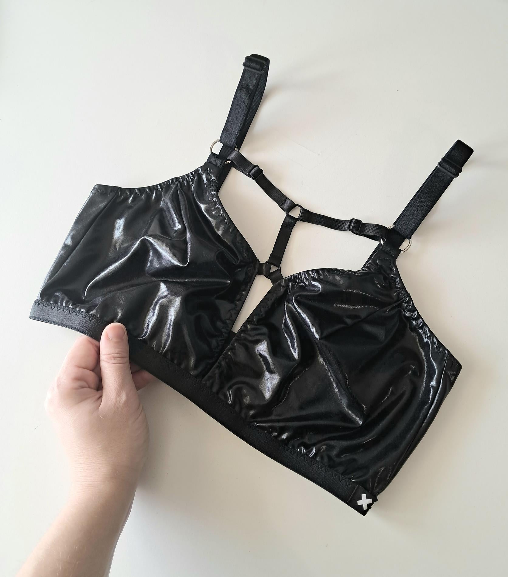 Black wet look bra  held by a hand on a light background