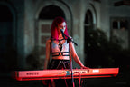 Person with red hair wearing wet look bra playing a KROSS keyboard in a dimly lit setting