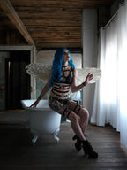Woman with blue hair with wet look bra sitting on a white bathtub in a rustic room.