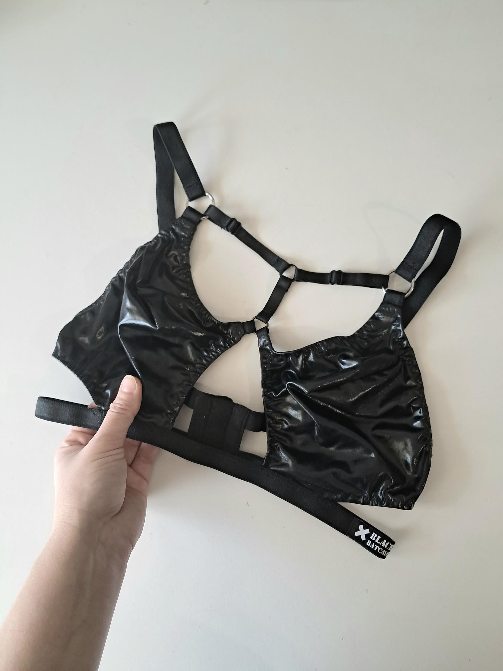 Black cut-out wet look bra held by a hand on a white background