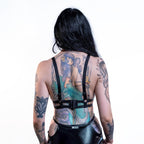 Person wearing a black cut-out wet look bra with visible tattoos on a white background