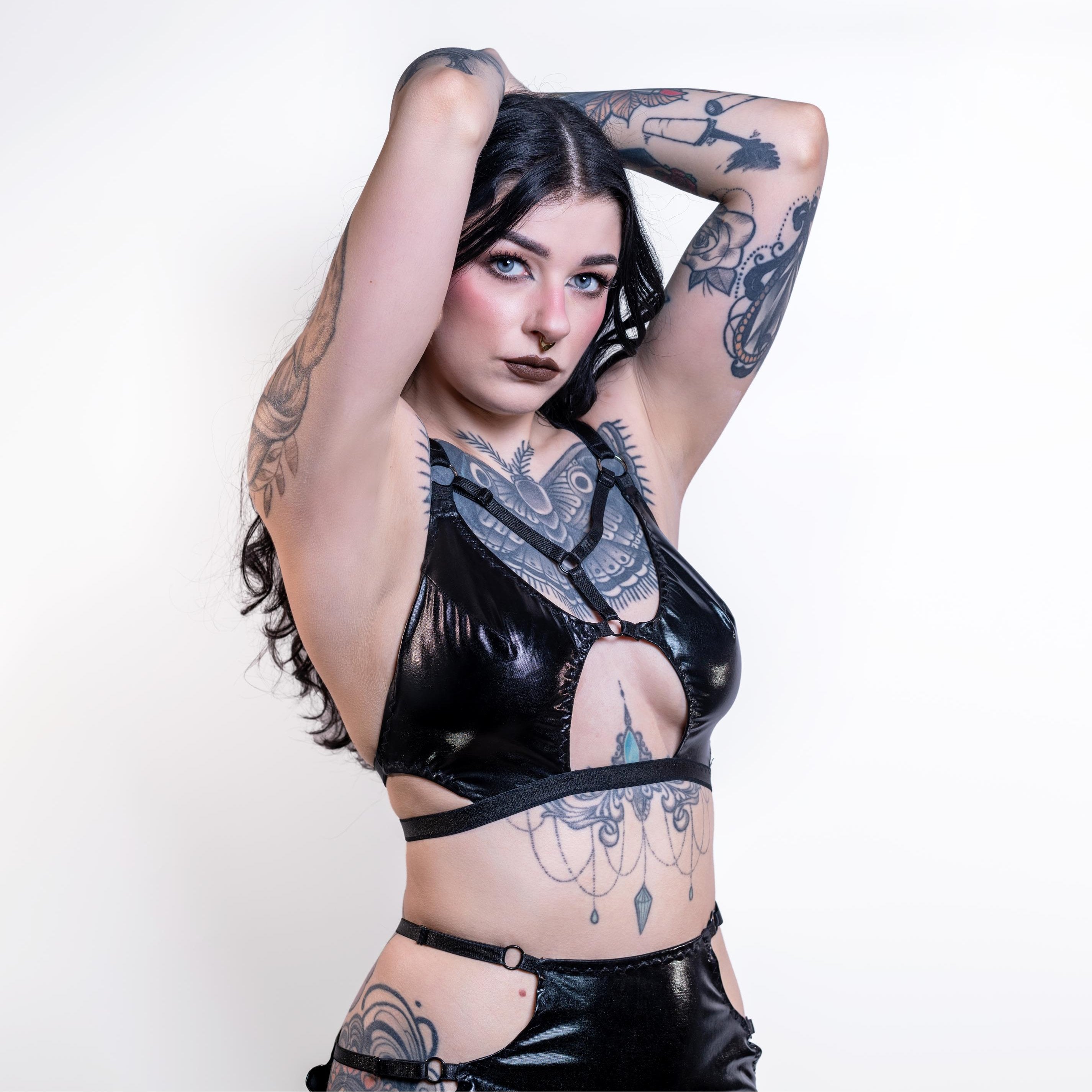 Woman wearing a black cut-out wet look bra with intricate designs on a white background