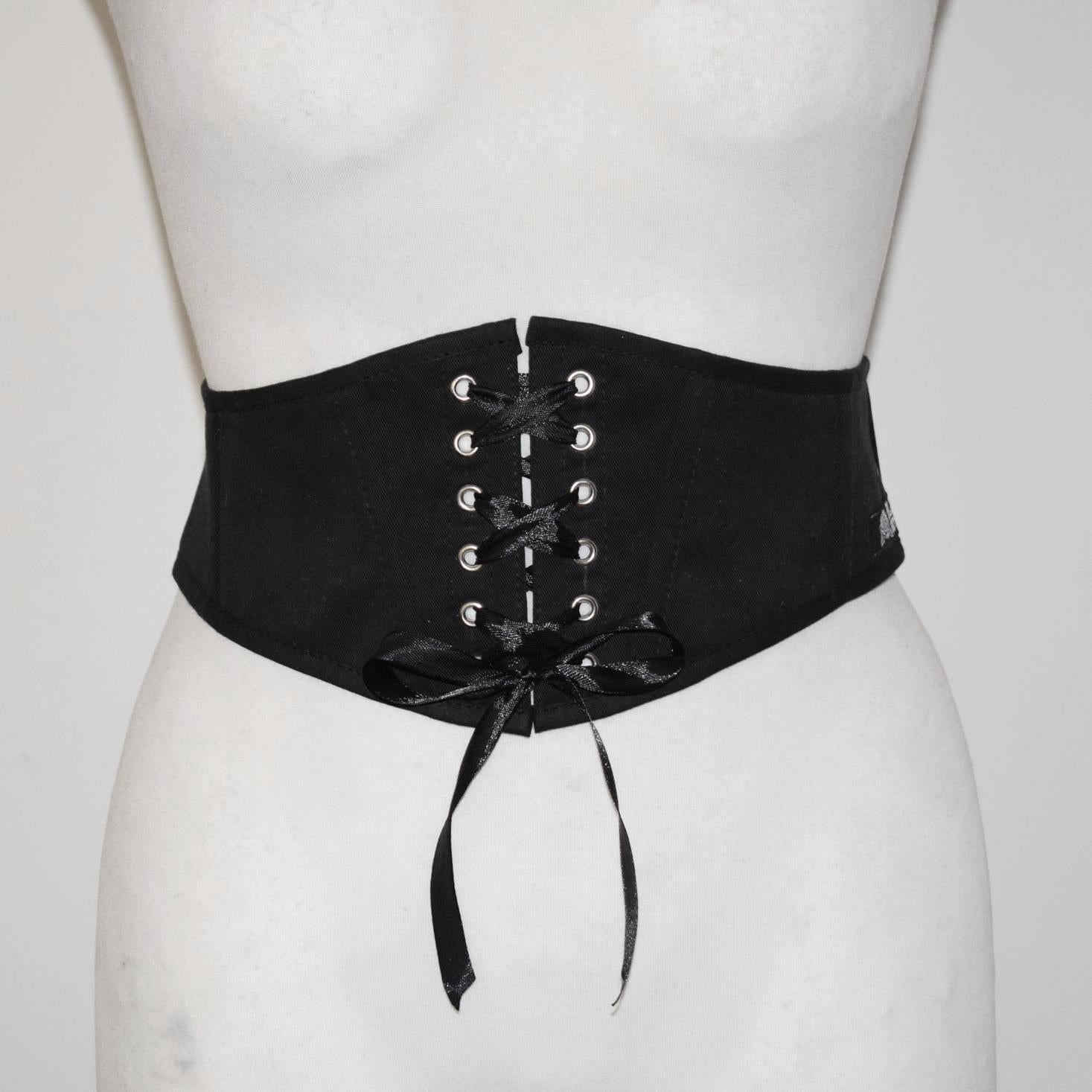Black corset belt with silver eyelets on a mannequin against a white background
