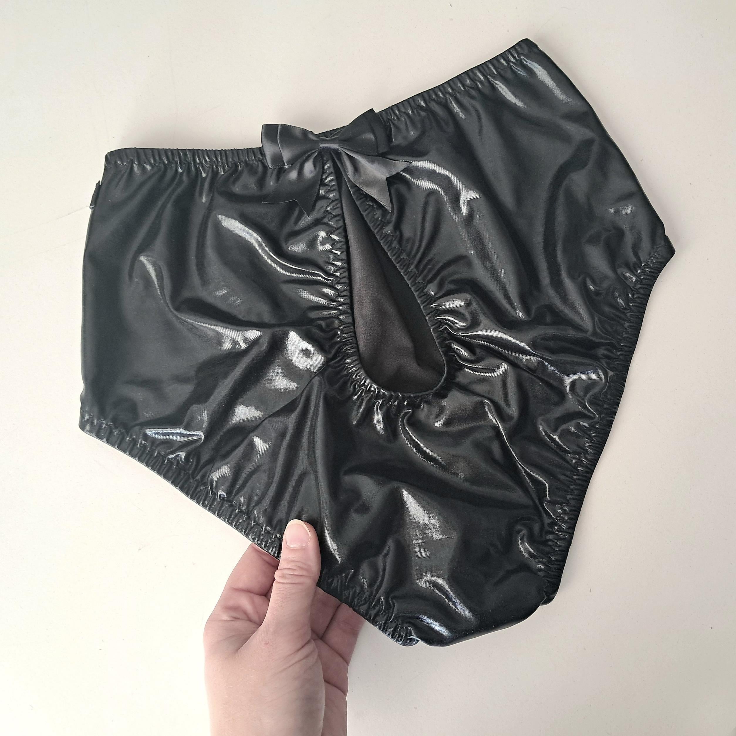 Black wet-look cut-out panties held by a hand against a plain background