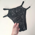 Black wet-look cut-out panties held by a hand on a white background