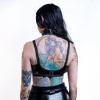 Person wearing a black open cup wet look bra with visible tattoos on a white background