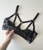 Black open cup wet look bra held by a hand on a light background