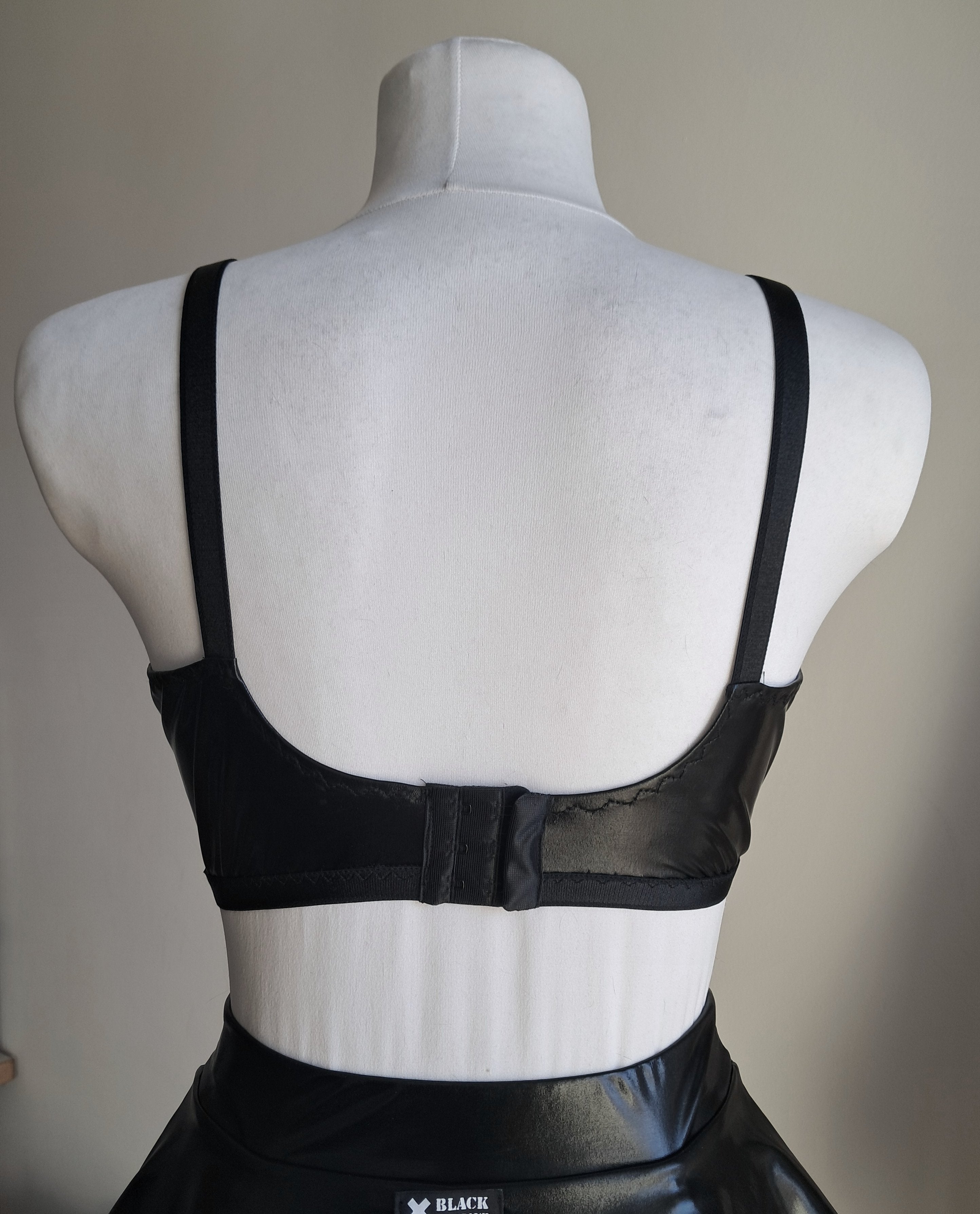 Black open cup wet look bra on a mannequin with a plain background