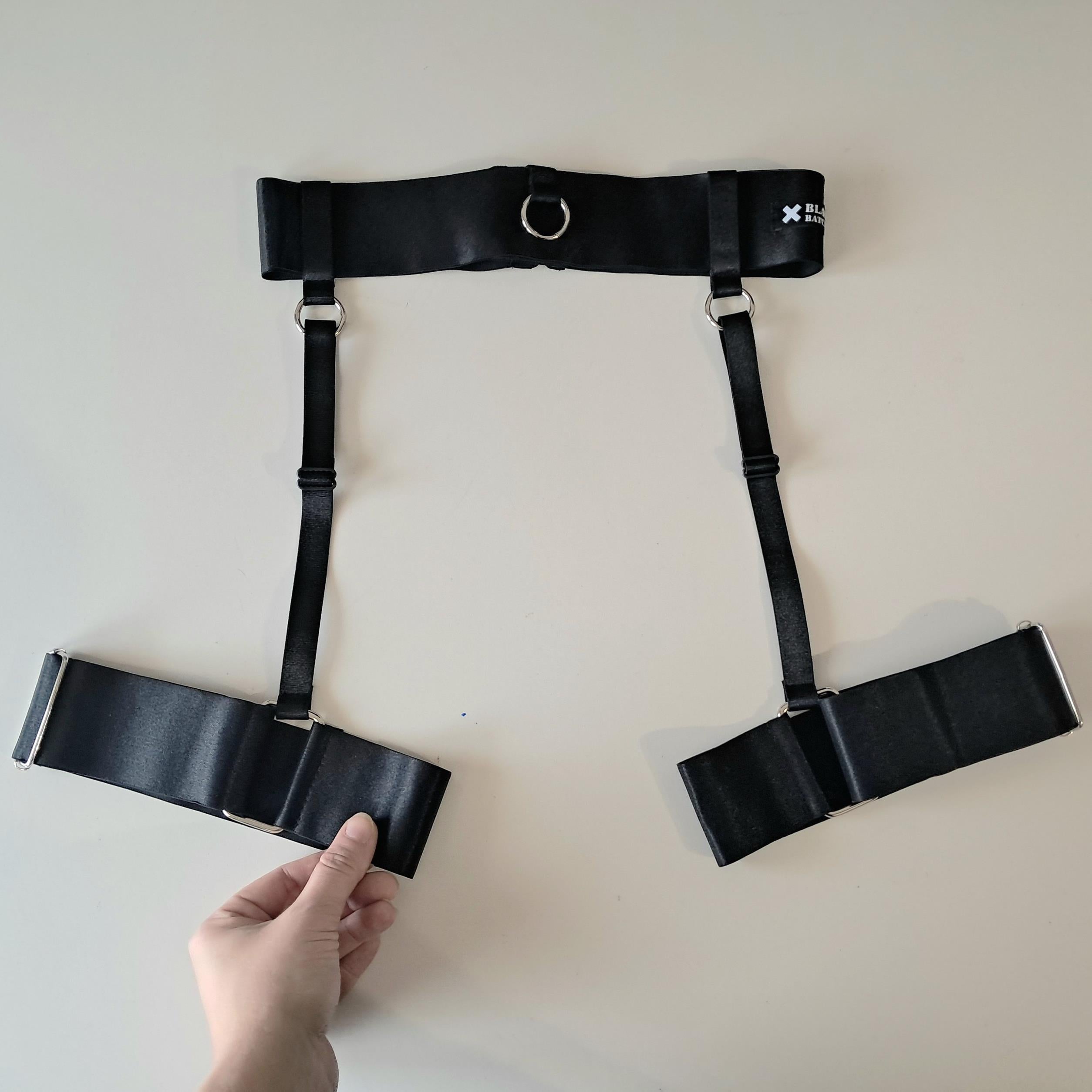 Black satin shine garter belt held by a hand on a light background