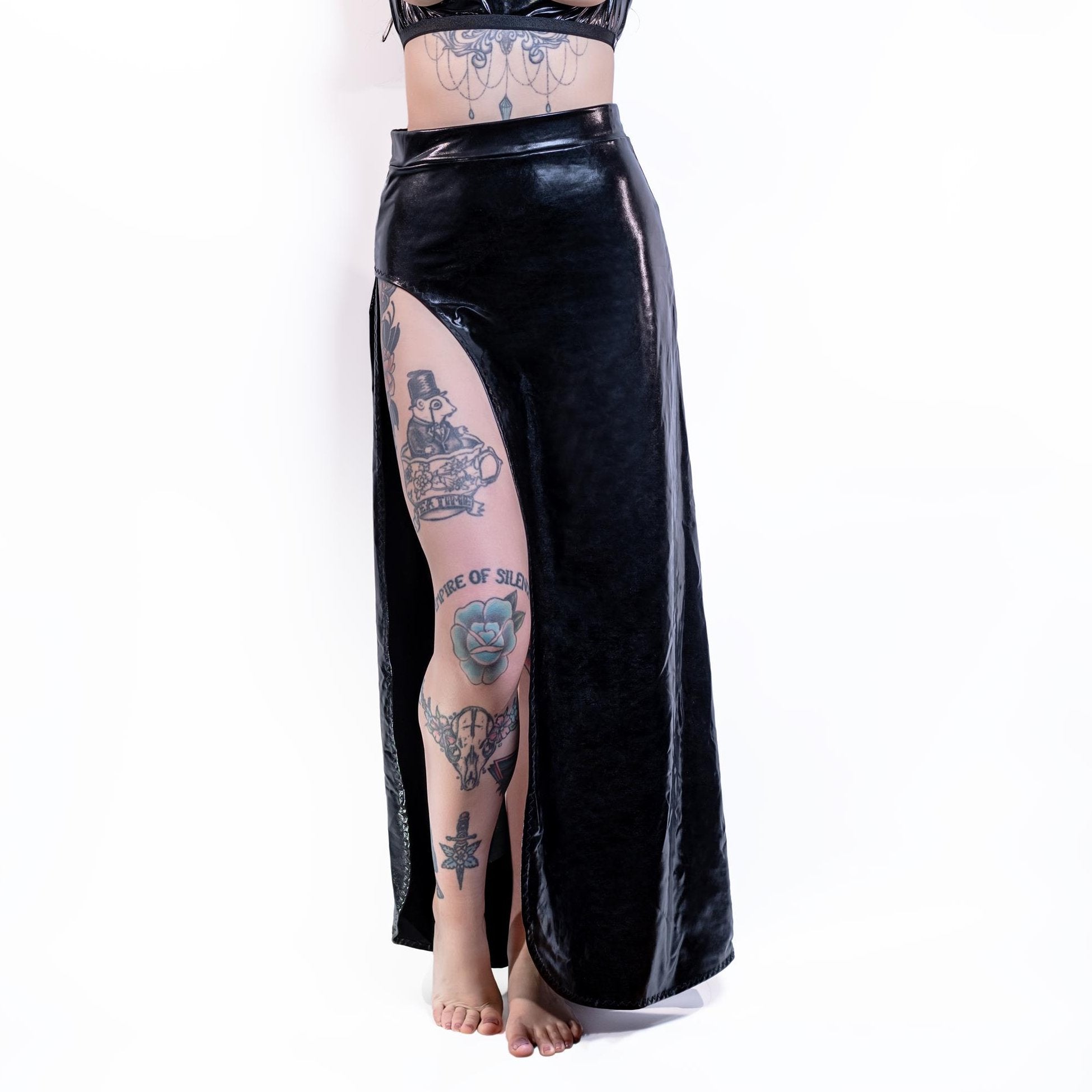 Person wearing a black wet-look cut-out maxi skirt with tattoos on a white background