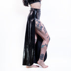 Person wearing a black wet-look cut-out maxi skirt with tattoos visible on the legs against a white background