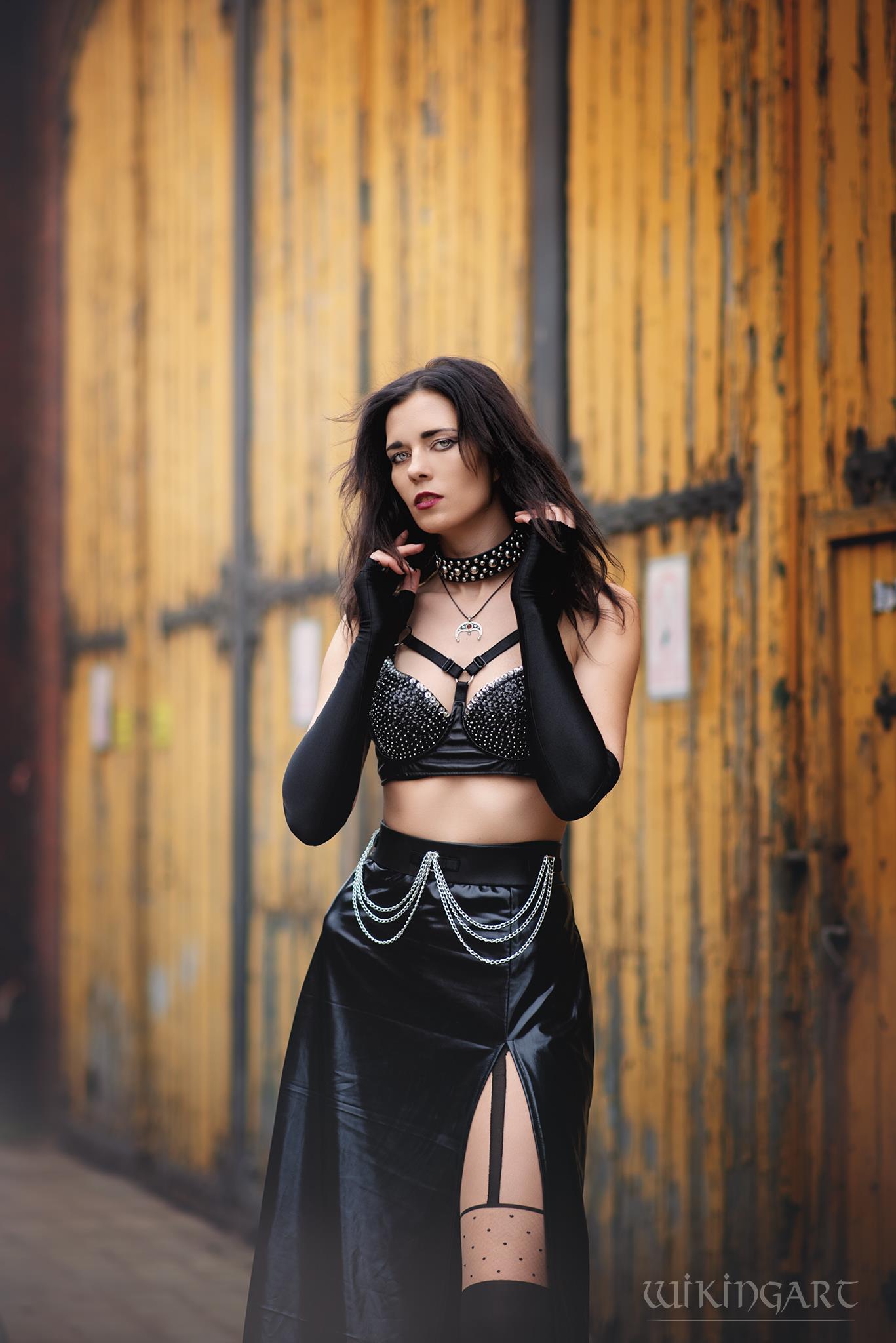 Woman in black wet-look cut-out maxi skirt standing against a wooden door background