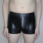 Person wearing shiny black leather shorts against a plain background