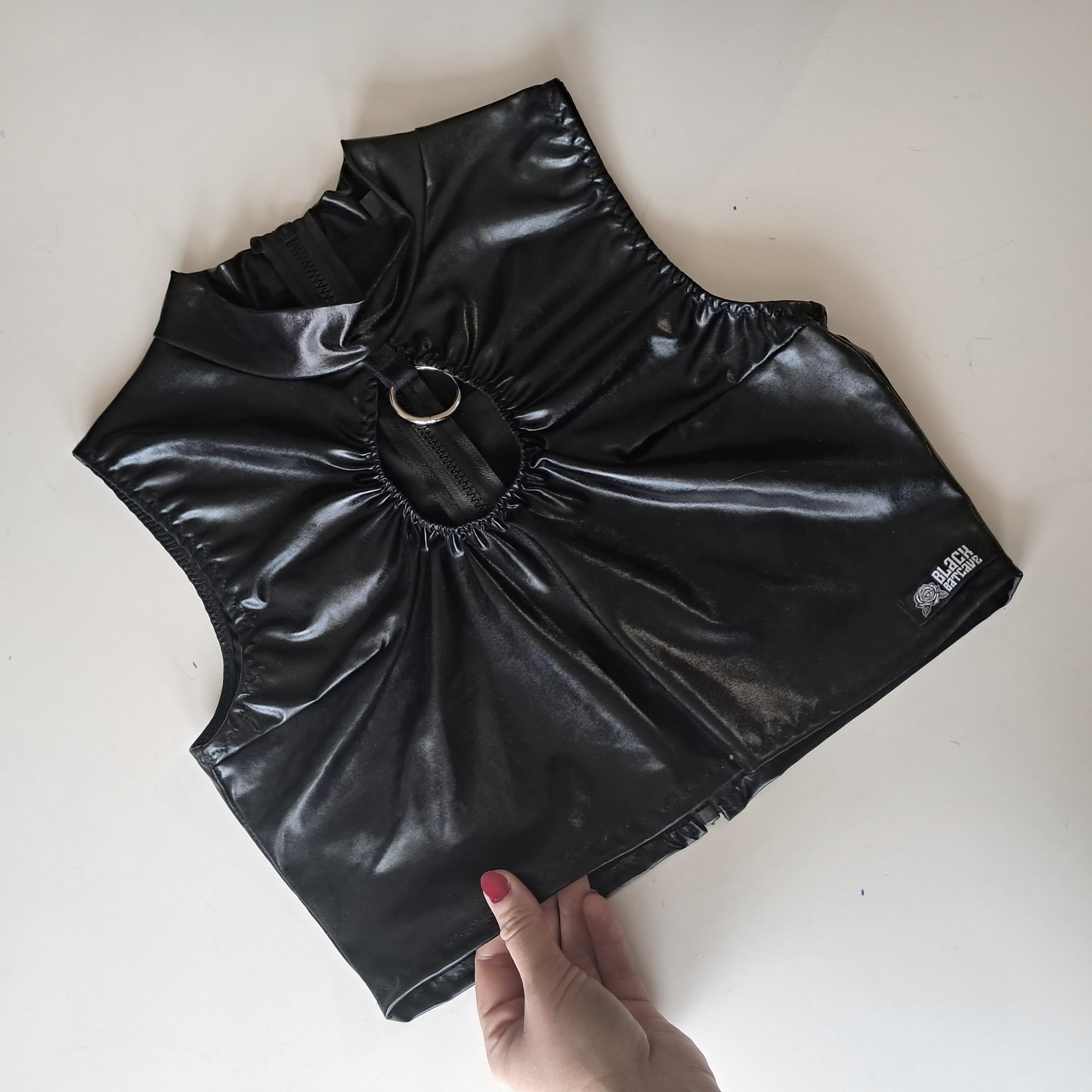 Black wet-look sleeveless crop top held by a hand on a white background