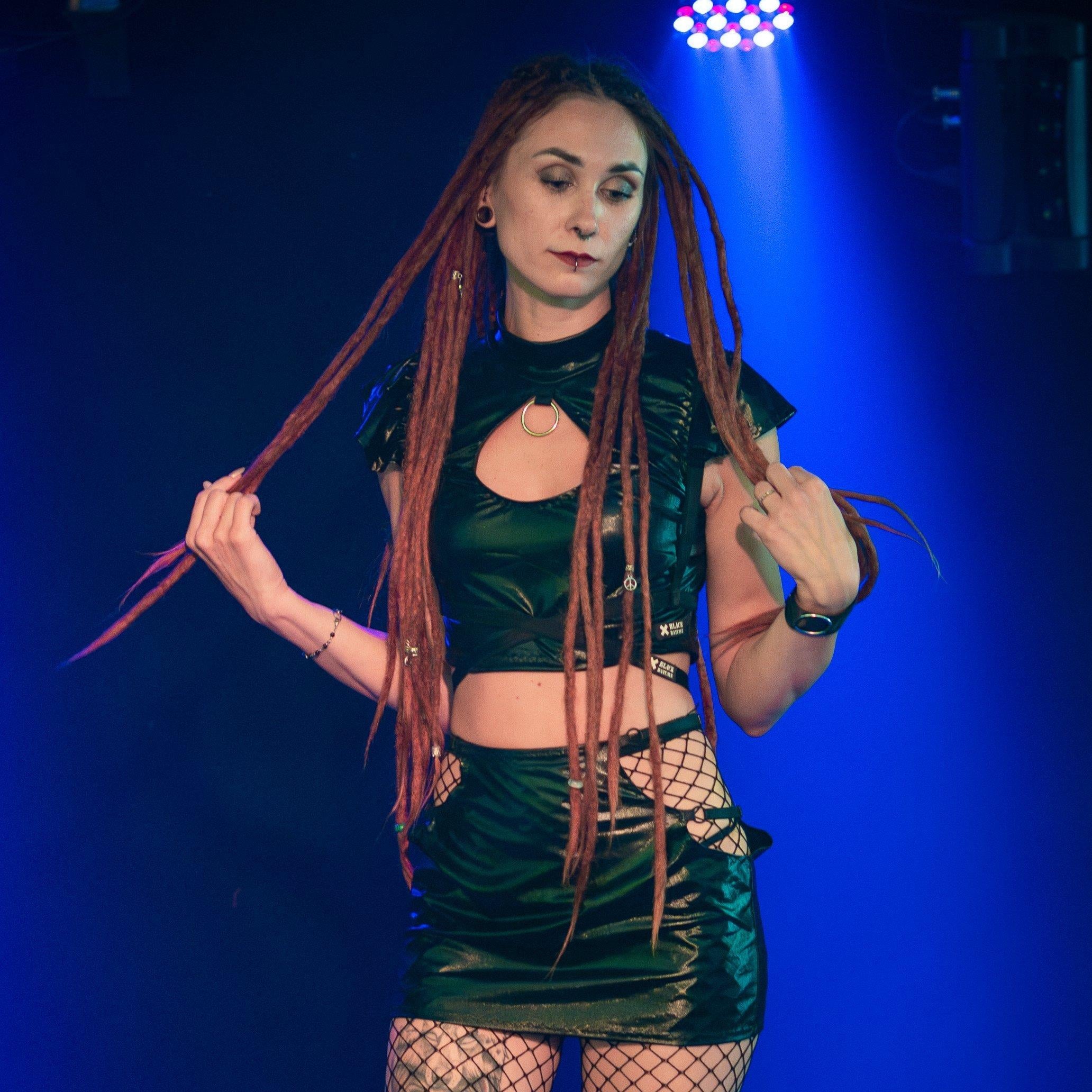 Woman with long braided hair wearing a wet-look sleeveless crop top on a stage with blue lighting