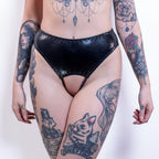 Person wearing black wet-look open crotch panties with tattoos on arms and legs against a white background