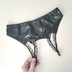 Black wet-look open crotch panties held by a hand on a white background