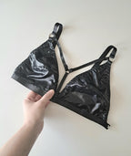 Black shiny wet look triangle bra held by a hand on a light background