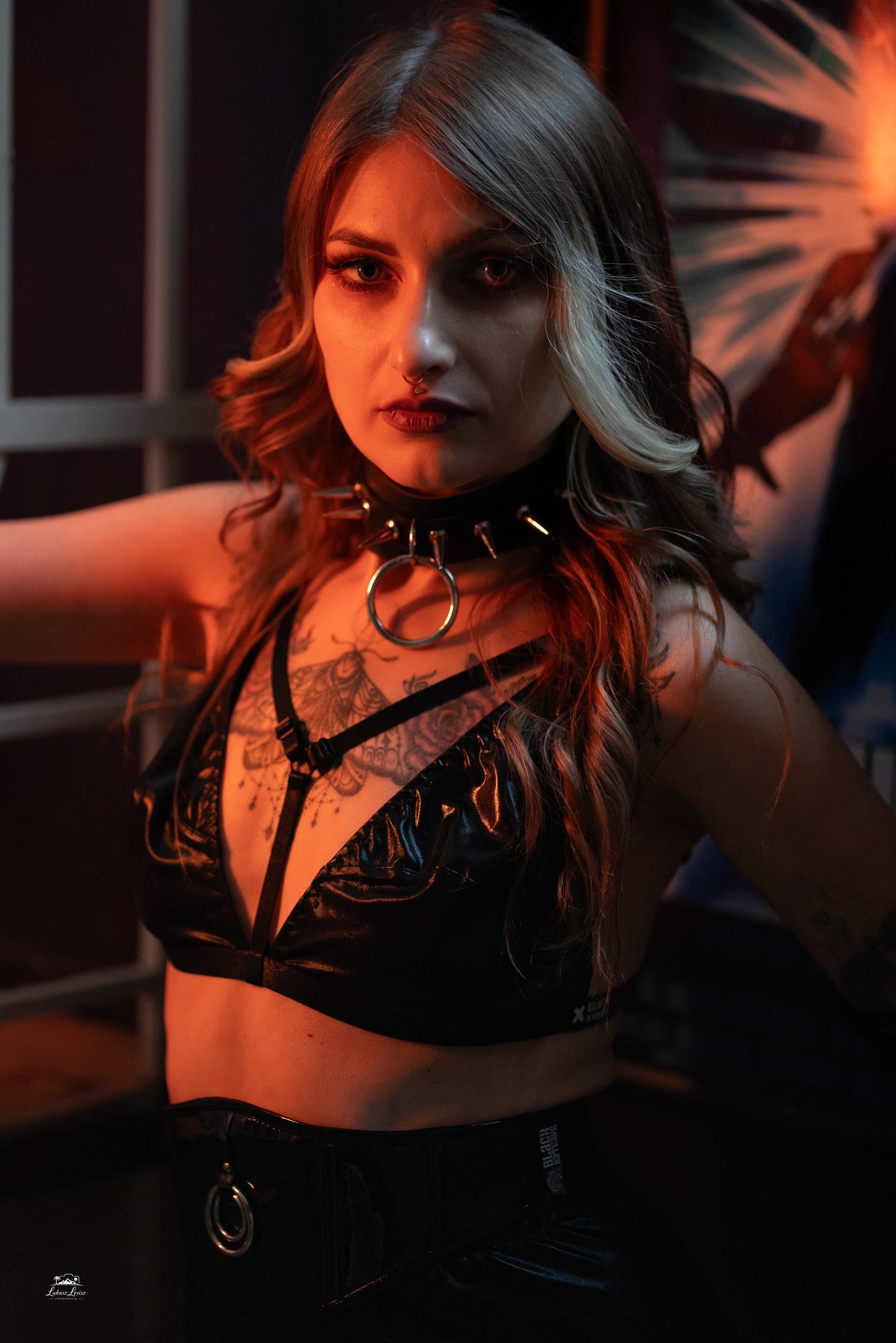 Person wearing a black wet look triangle bra with intricate designs, sitting against a dark background.