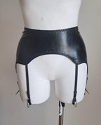 Black wet look garter belt on a mannequin against a plain background