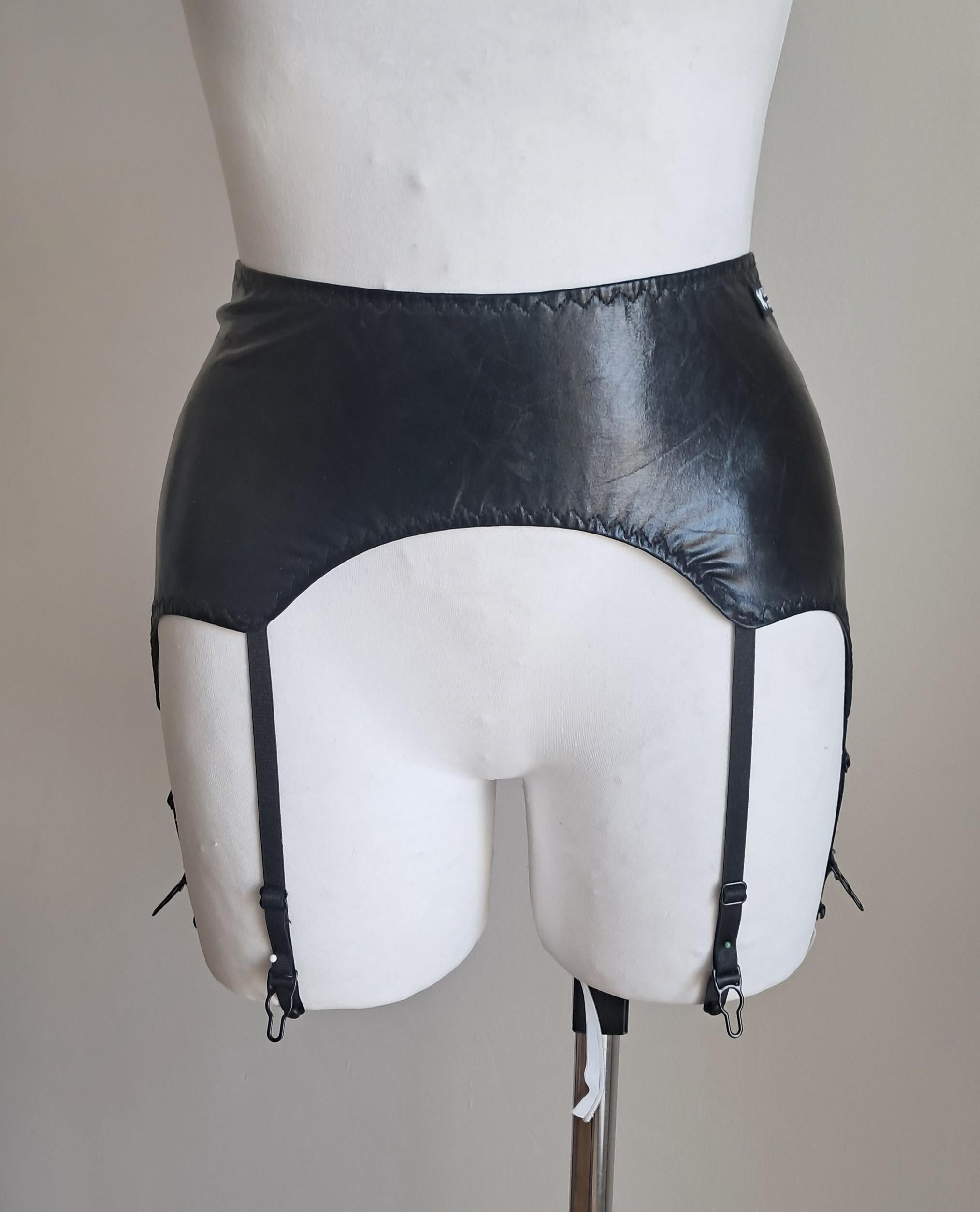 Black wet look garter belt on a mannequin against a plain background
